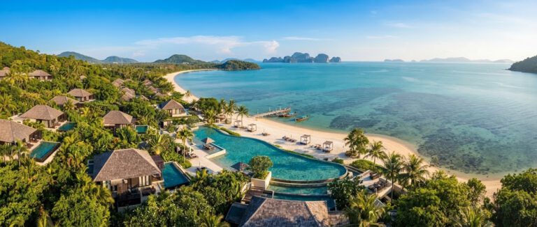 Panoramabild im Querformat eines luxuriösen Strandresorts auf Koh Samui, Thailand. Das Foto zeigt eine traumhafte Bucht mit weißem Sandstrand, türkisfarbenem Wasser, einem einladenden Poolbereich und eleganten Villen, eingebettet in üppige tropische Natur und Palmen.